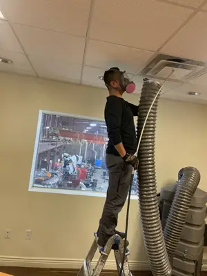 Technician on a ladder connecting duct-cleaning equipment to a ceiling register
