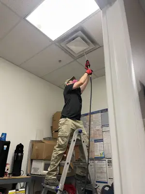 Technician working on a ceiling supply vent during commercial duct cleaning